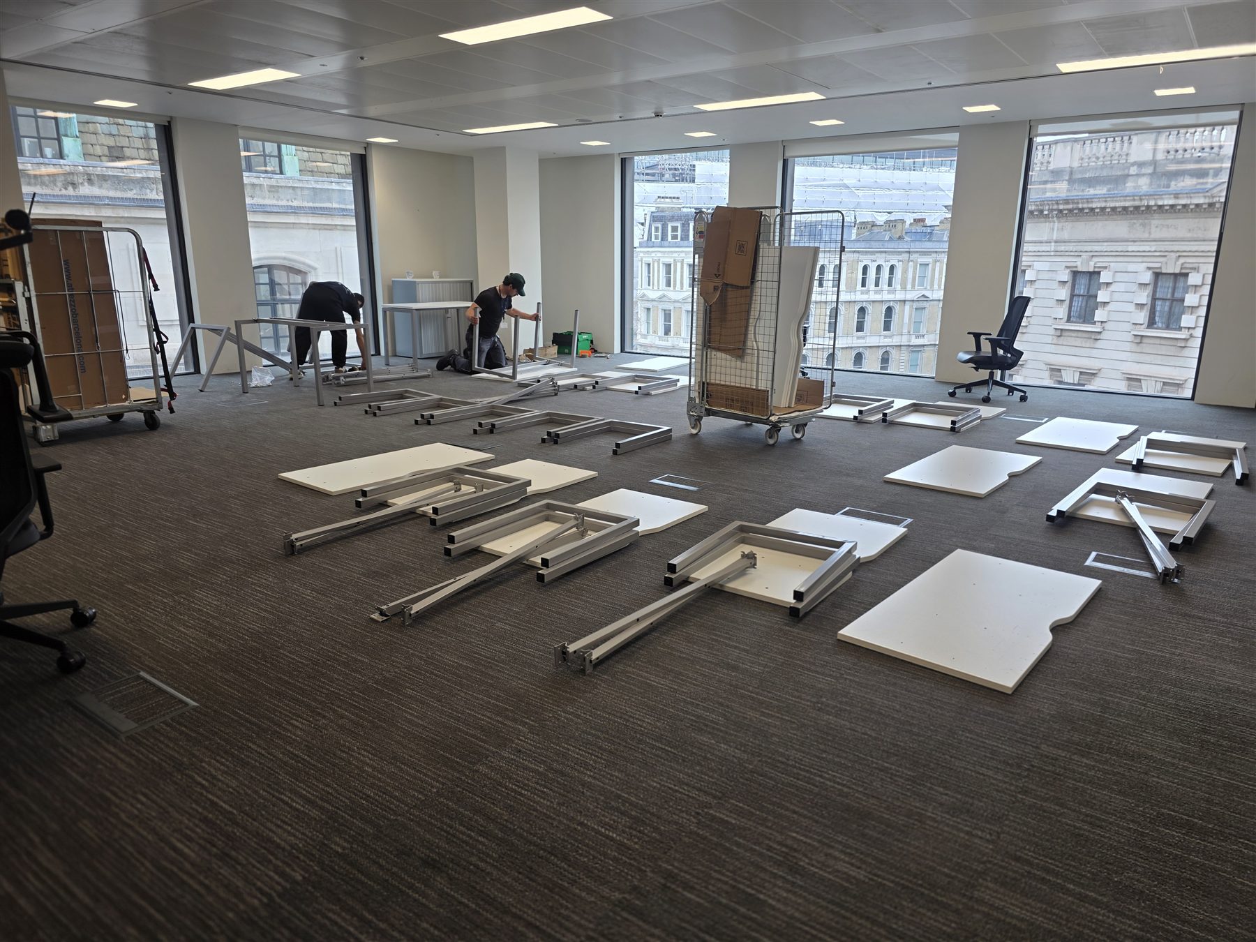 Oneplace2save team working with dismantled desks and furniture trolleys in a bright office.