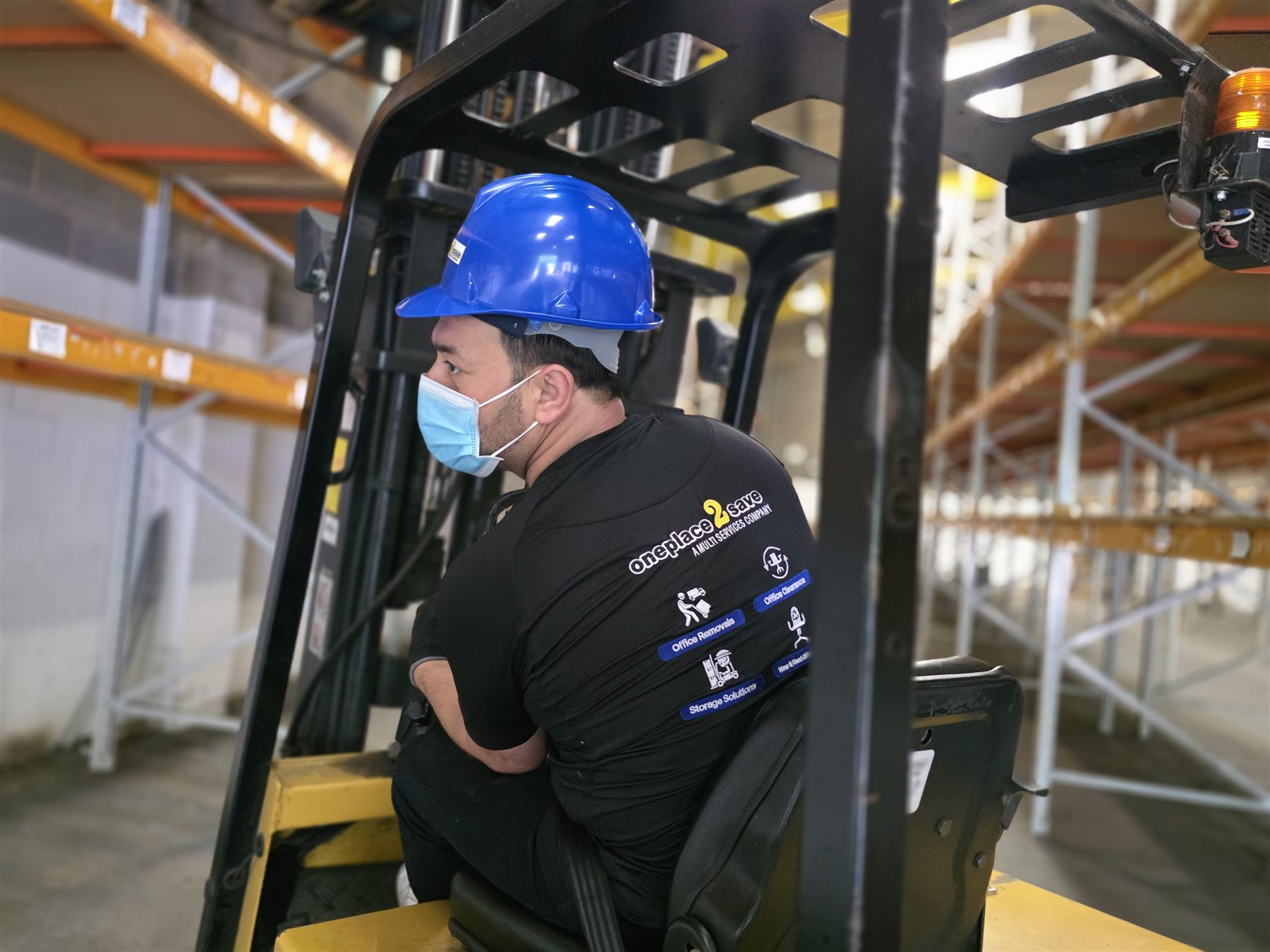 Oneplace2save forklift operator wearing a blue hard hat inside a storage warehouse.