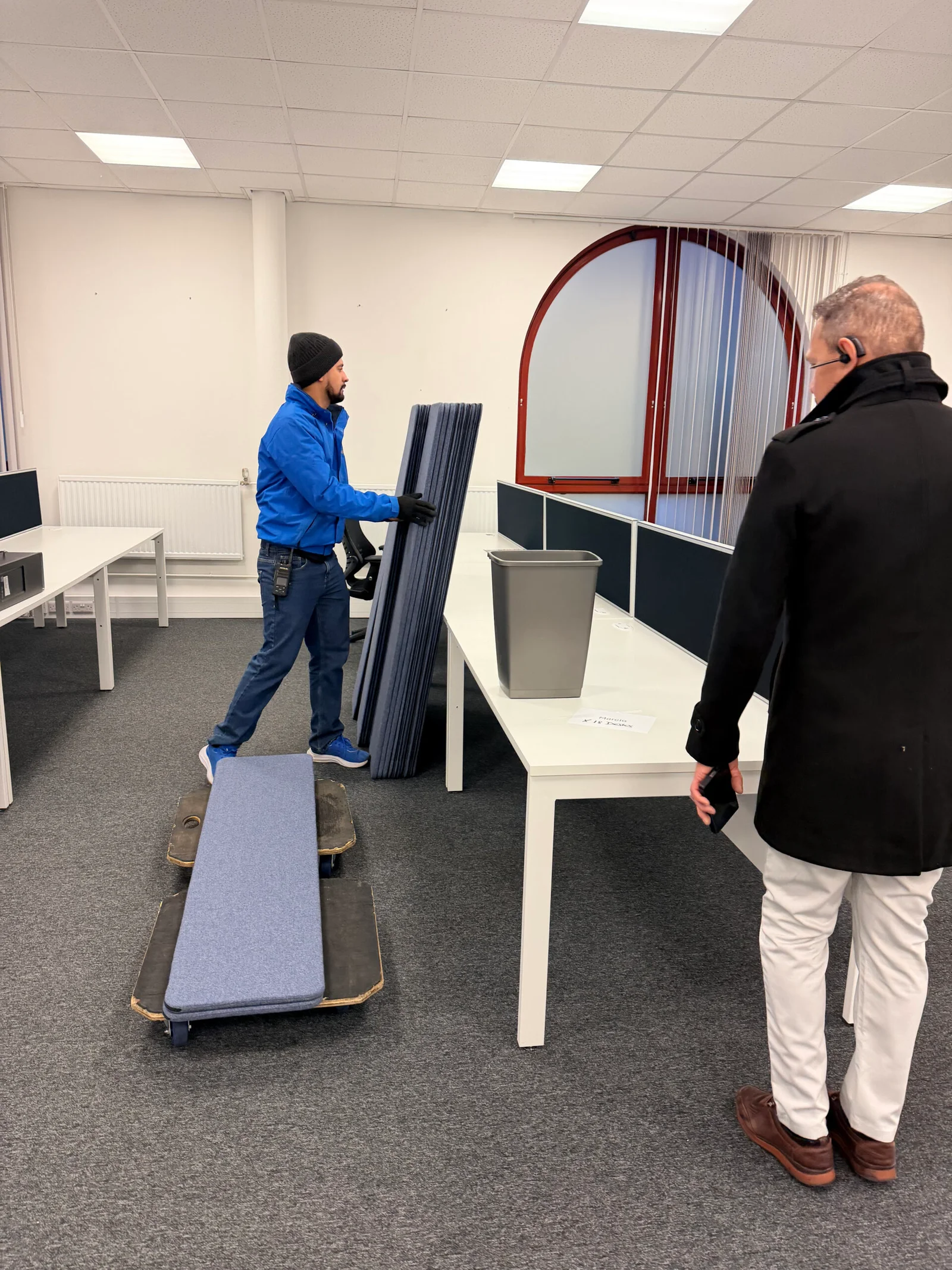 A Oneplace2save crew member handling office partition panels beside desks.