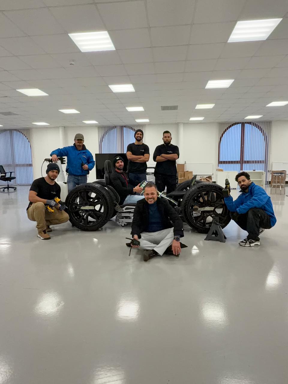 Oneplace2save team gathered around the office-chair F1 pit-stop setup after completing work at the McLaren site.