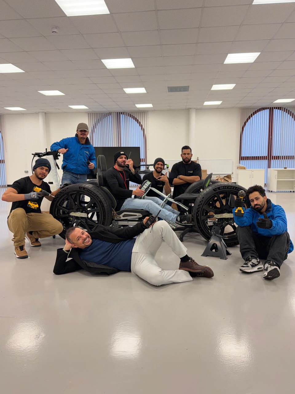 Oneplace2save team posing with genuine McLaren wheels and their office-chair pit-stop setup after completing relocation work.